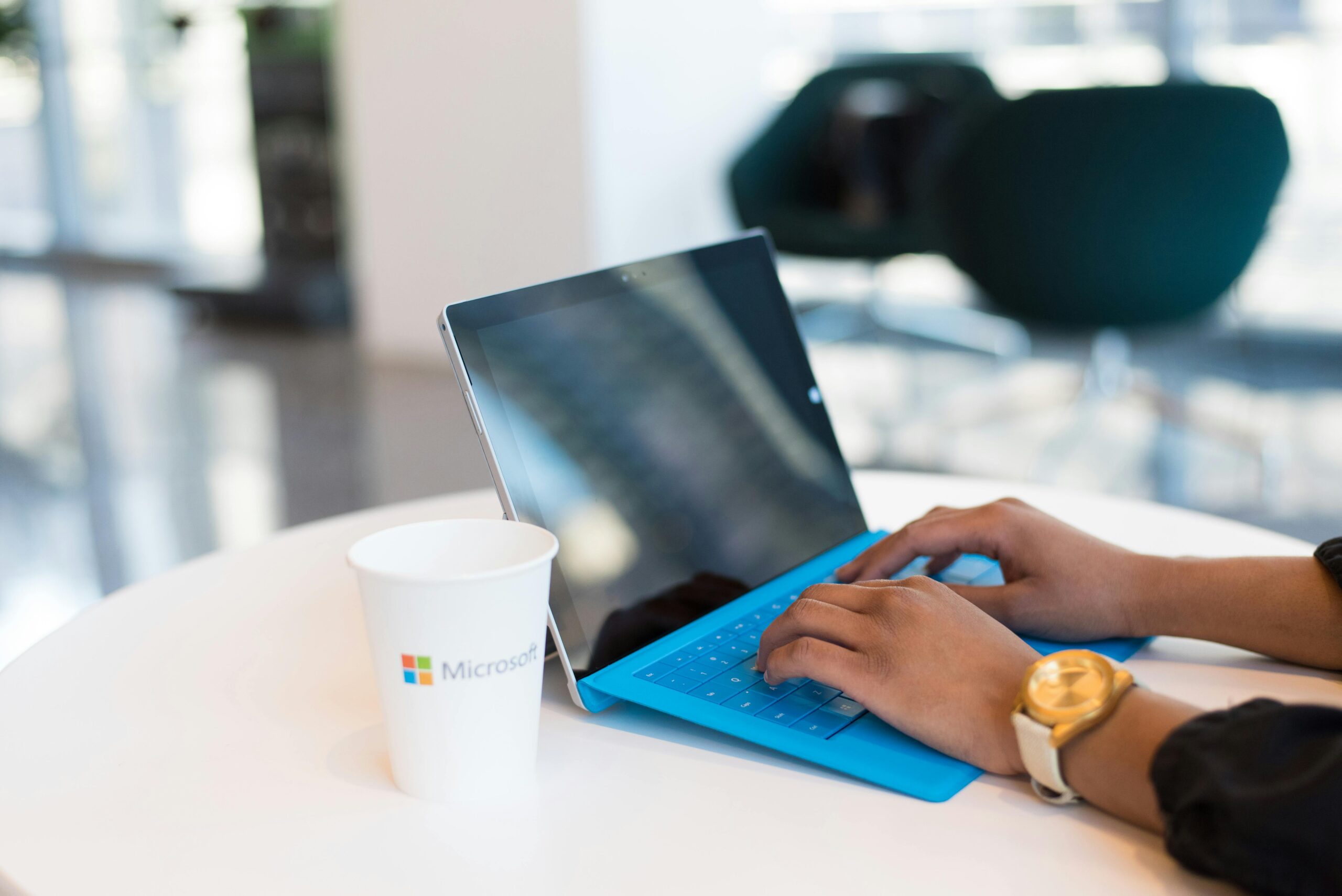 Hands typing on a blue keyboard with a branded cup on a table.